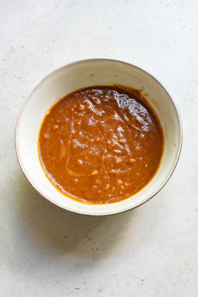 A white bowl filled with a thick, brown sauce placed on a light-colored surface. The texture of the sauce appears smooth with some visible small lumps.