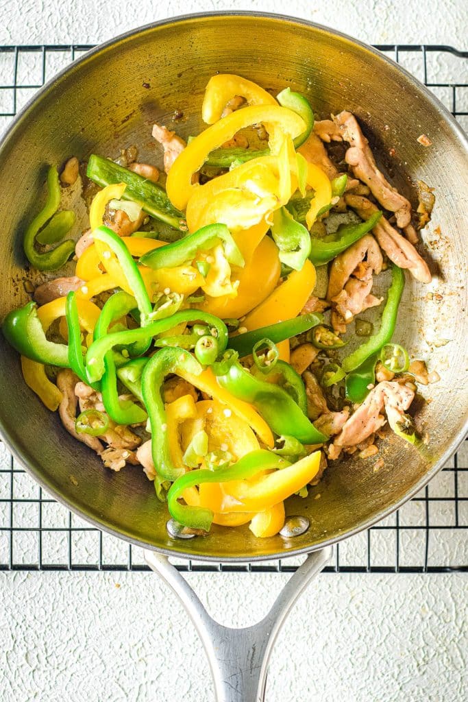 A skillet filled with sliced yellow and green bell peppers, cooked with strips of meat. The ingredients are sautéed and arranged on a cooling rack with a light background.