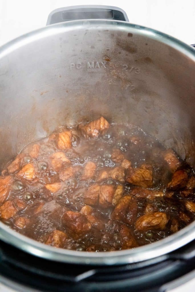An Instant Pot with a savory beef stew cooking inside. The pot is filled with chunks of beef simmering in a rich, brown sauce. The interior of the Instant Pot is slightly fogged up due to the steam.
