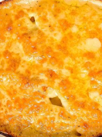 A close-up of a baked dish with a golden-brown crust, possibly cheesy or creamy. The dish is round and placed on a striped cloth, with edges slightly toasted, suggesting a gratin or casserole.