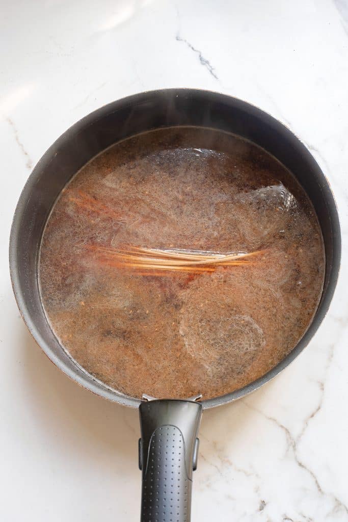 A pot on a marble countertop containing a simmering broth with visible streaks of oil on the surface. Steam is rising from the pot, suggesting the broth is hot.