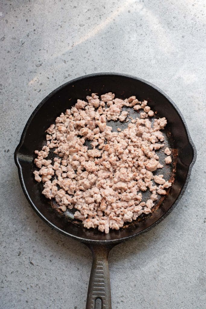 A black frying pan on a gray countertop contains cooked ground meat. The meat is browned and crumbly, evenly spread across the pan.
