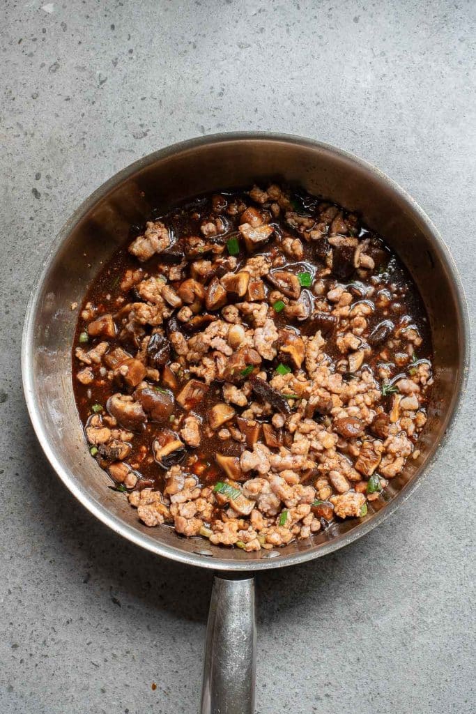 A metal pan filled with cooked ground meat mixed with diced vegetables and a dark sauce, placed on a gray countertop.
