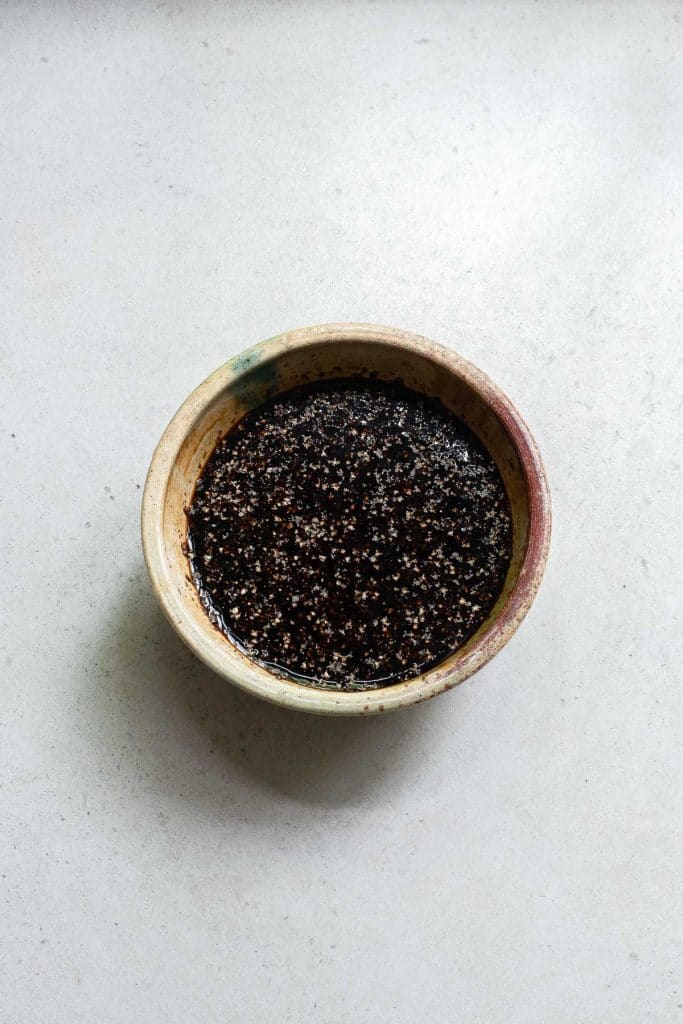 A small bowl filled with a dark, seasoned mixture of spices on a light gray surface.