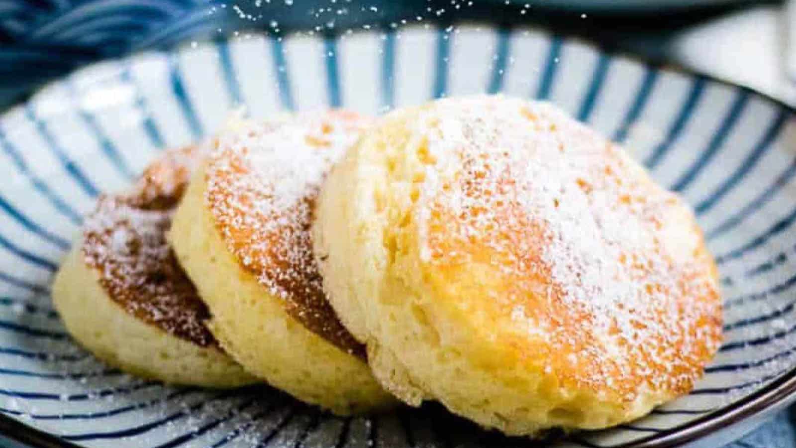 Three souffle pancakes with powdered sugar on a blue and white striped plate.