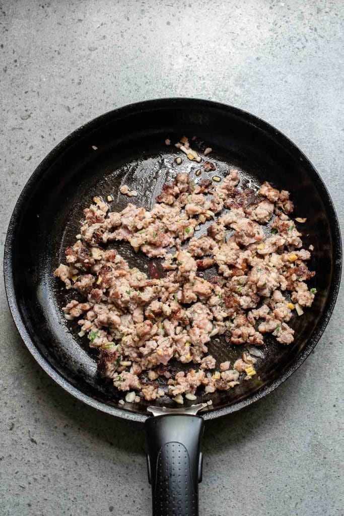 A black frying pan on a stone countertop contains cooked ground meat with minced onions and herbs mixed in.