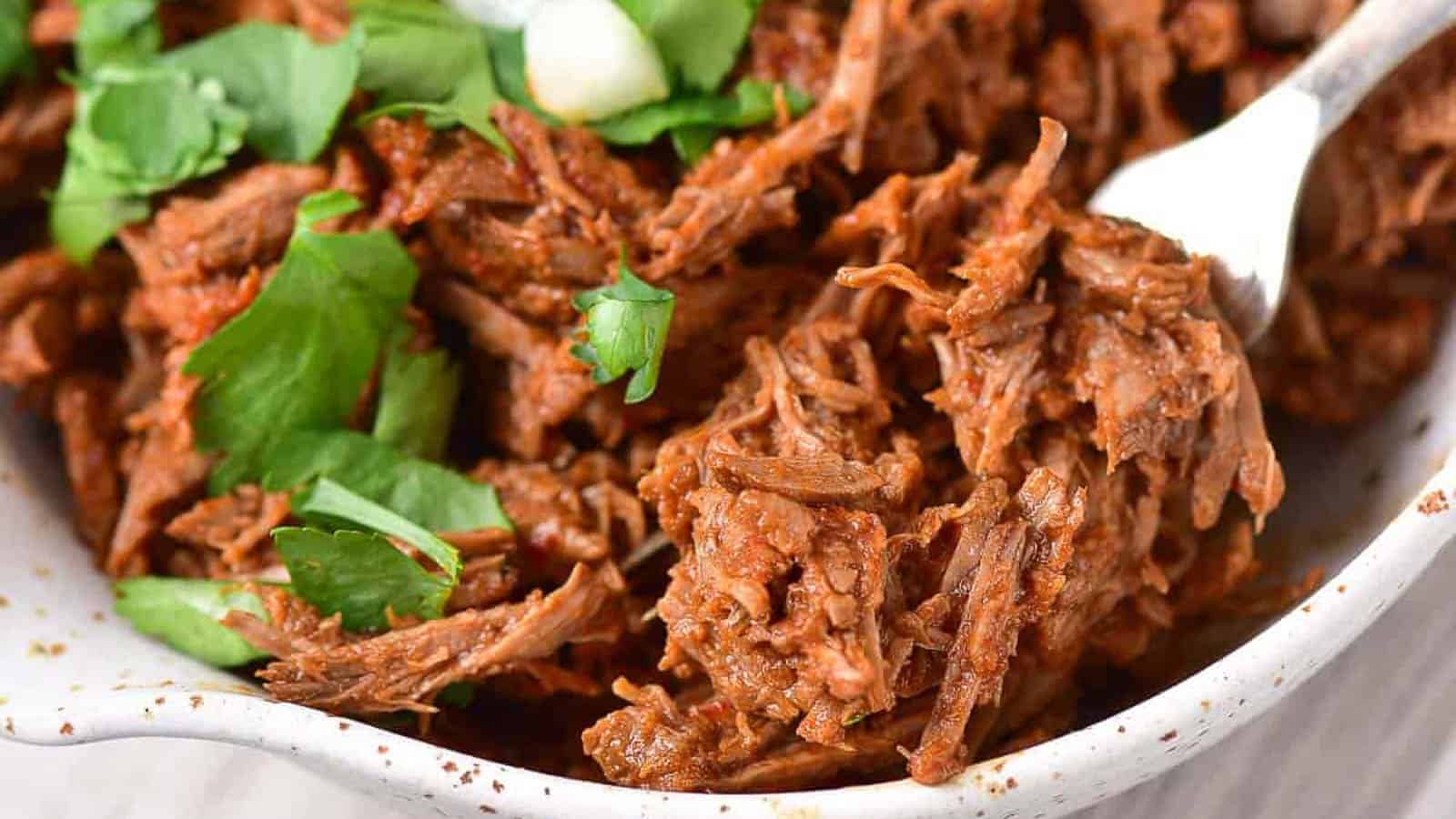 low angle shot of shredded beef in a bowl with a fork.