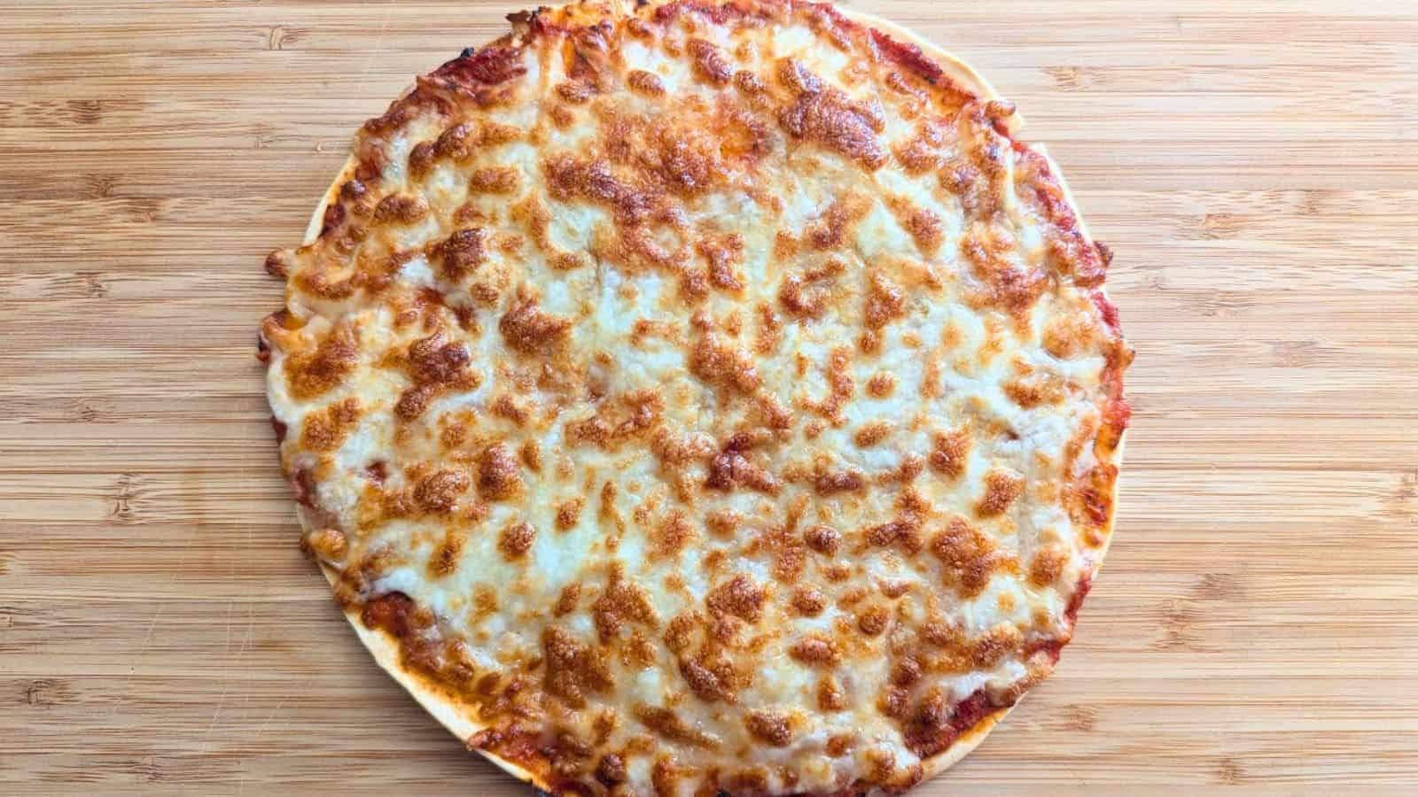 A whole cheese pizza with a golden, bubbly melted cheese topping sits on a wooden surface.