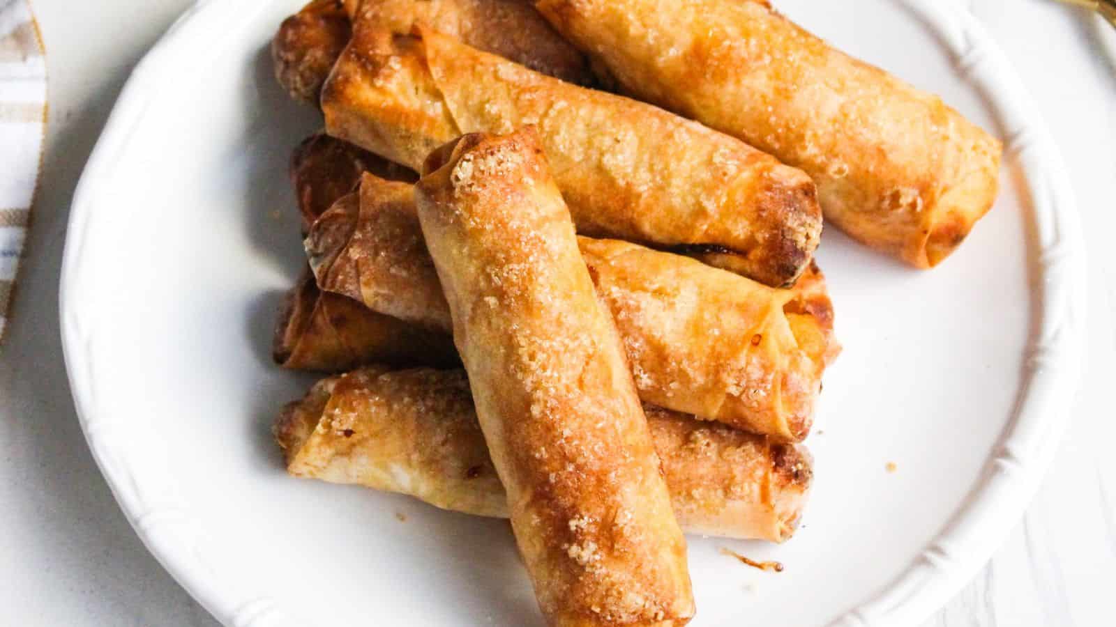 A white plate with a stack of golden-brown, crispy lumpia (Filipino spring rolls) arranged neatly on top of each other.
