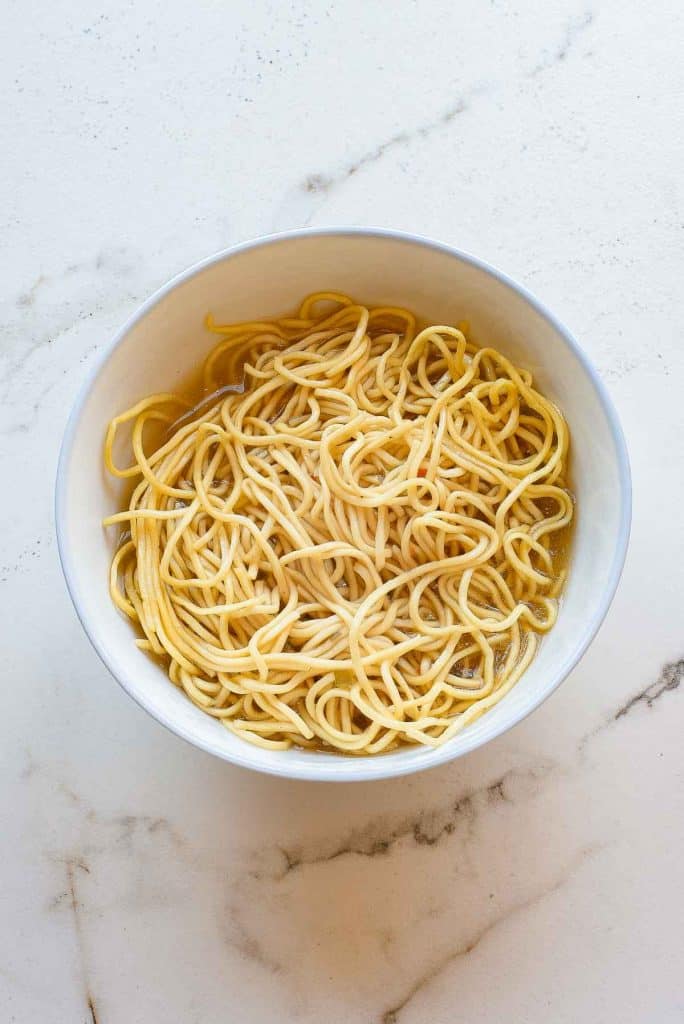 A white bowl filled with cooked plain spaghetti noodles sits on a white marble surface.