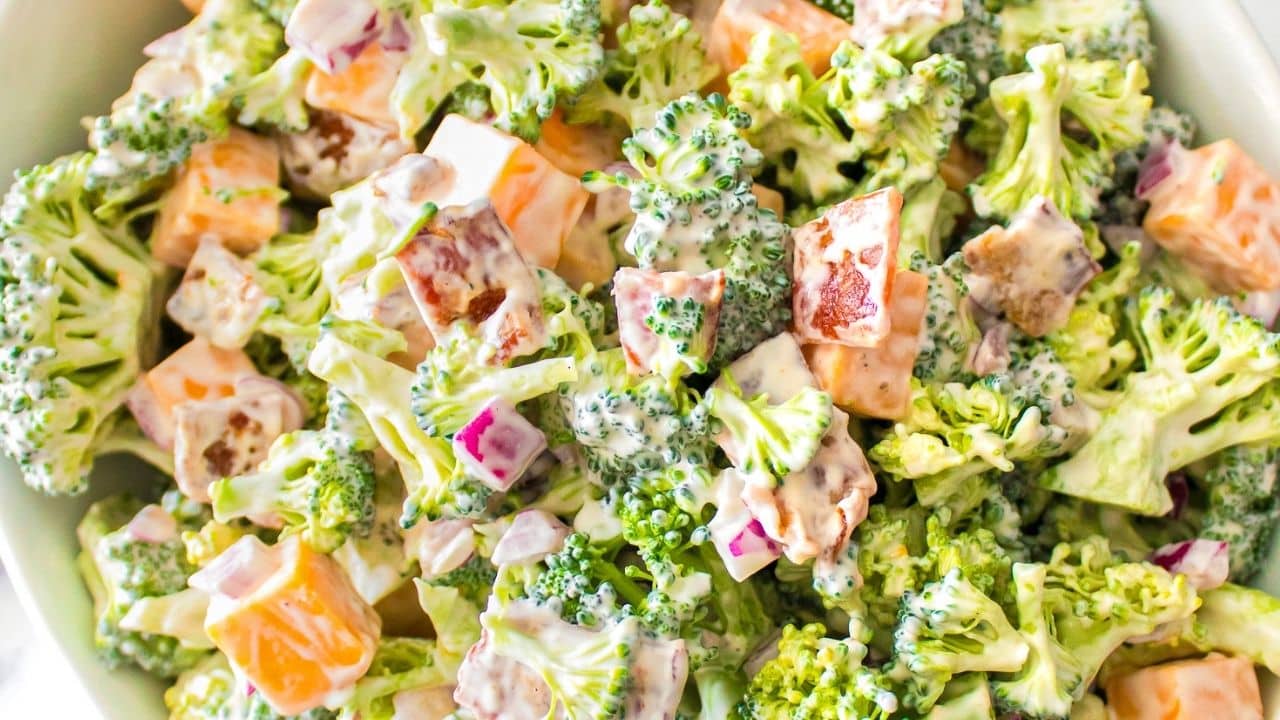 A creamy broccoli salad featuring tender florets, diced cheddar, red onions, and crispy bacon pieces, all coated in a luscious dressing.