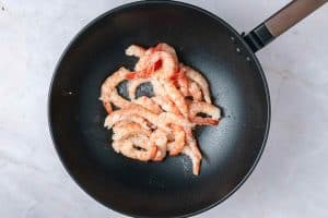 Cooked shrimp arranged in a pile inside a black wok pan, placed on a light marble surface.